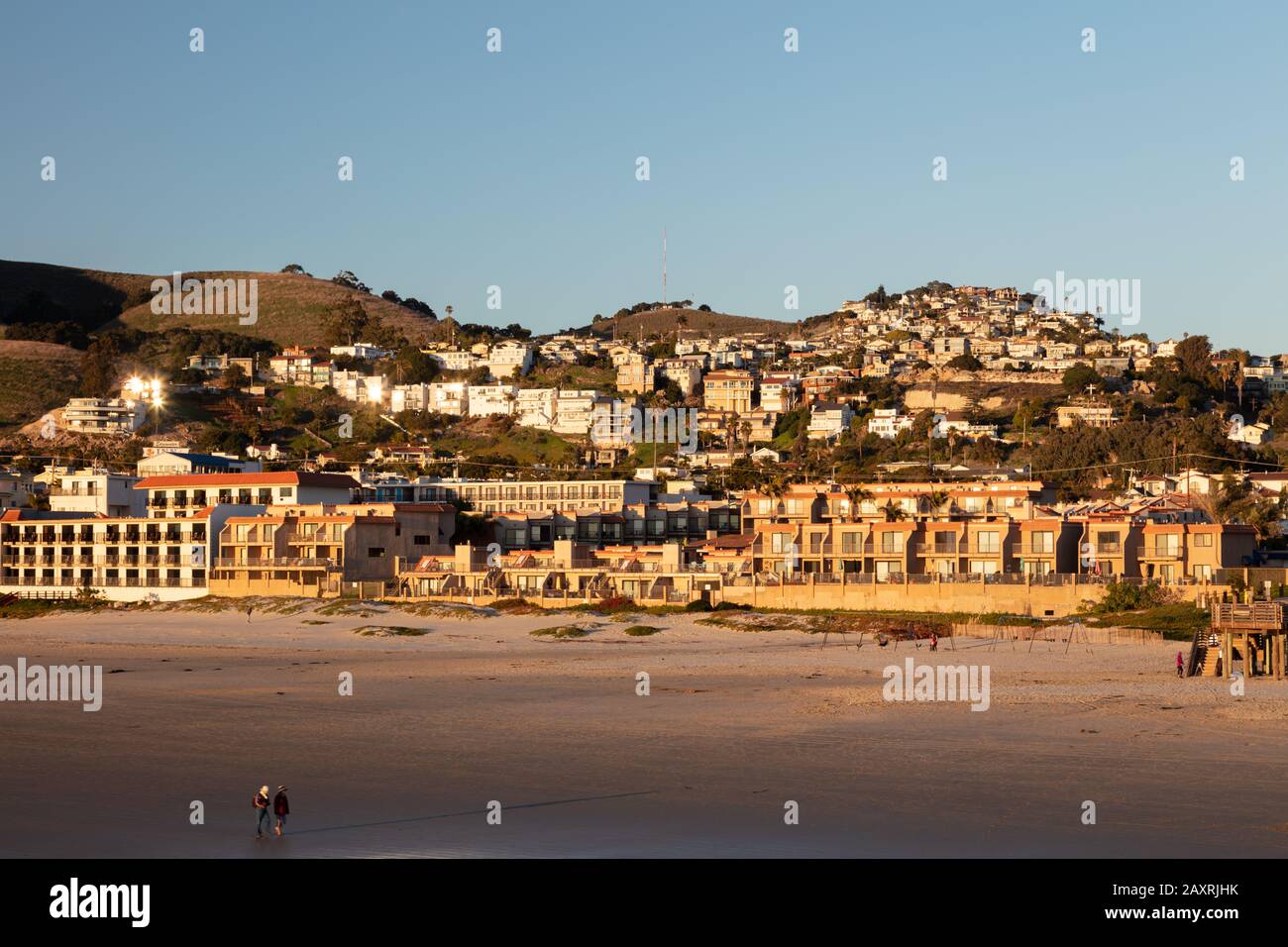 Vue sur la plage du centre-ville de Pismo depuis la promenade au coucher du soleil. De nombreuses maisons et entreprises sont présentées à la lumière du soleil en regardant l'océan. Banque D'Images