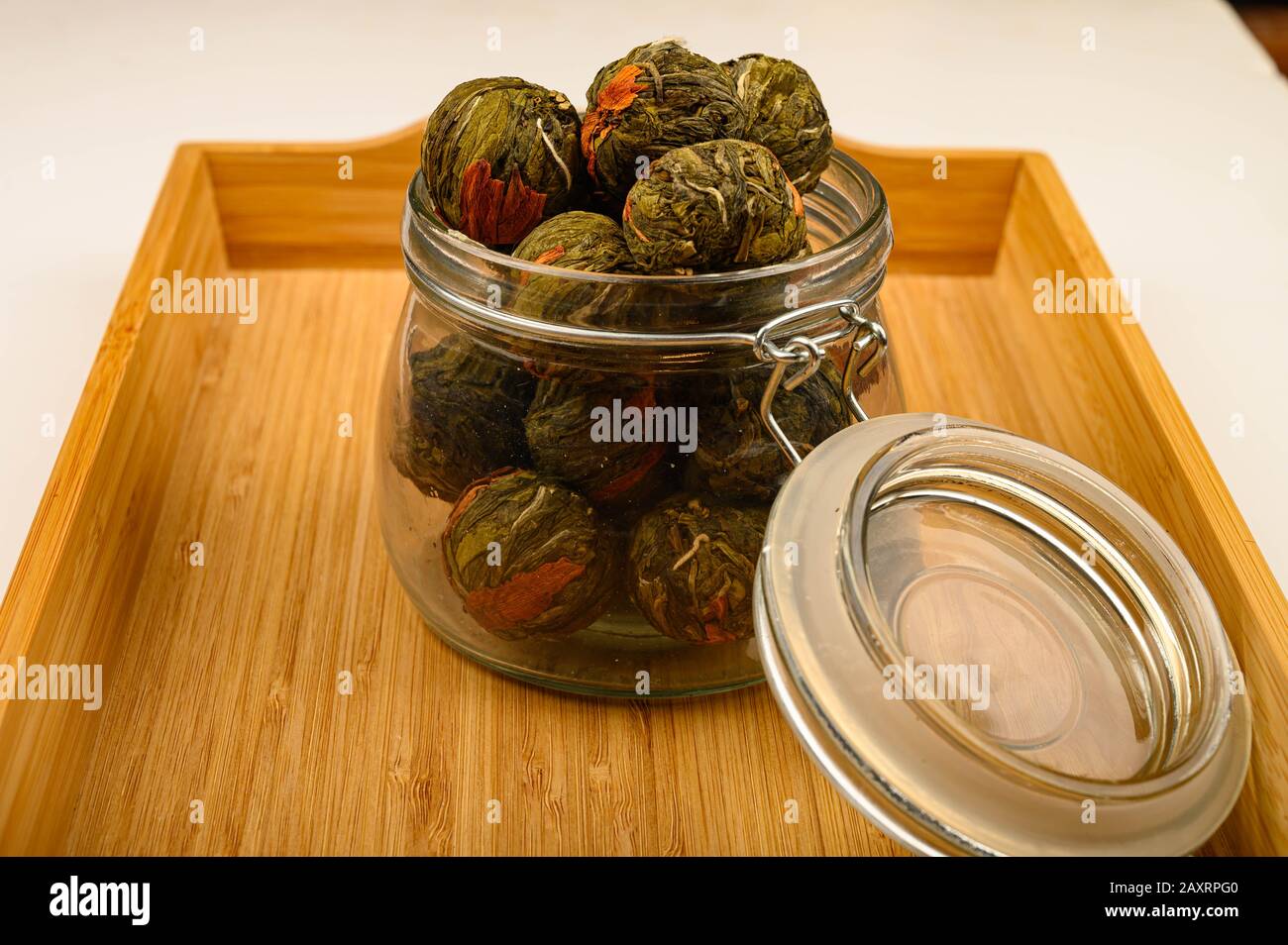Une boule de thé de fleur dans un pot en verre sur un plateau en bois sur un fond blanc. Gros plan Banque D'Images