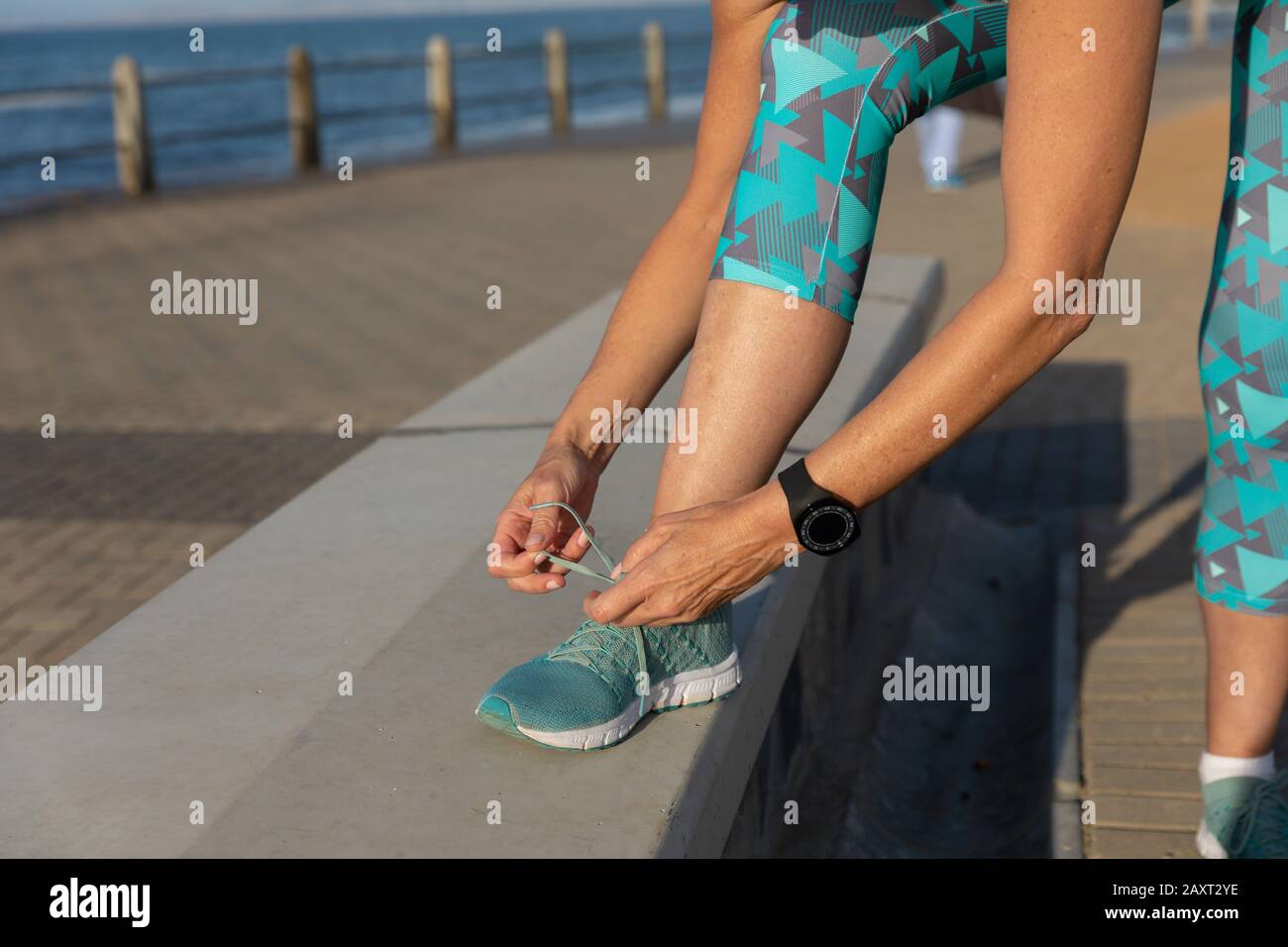 Gros plan sur la partie moyenne d'une femme caucasienne d'âge moyen mûre qui travaille sur une promenade, se courbant, nouant ses lacets de chaussures Banque D'Images