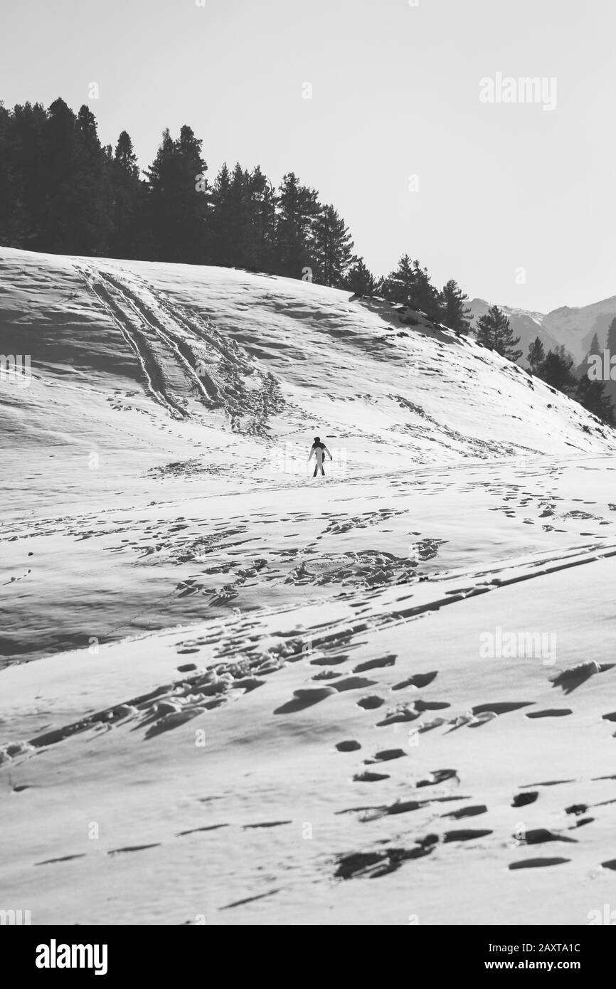 Une photo en noir et blanc d'un homme qui marche en montée à travers une partie de neige. Banque D'Images