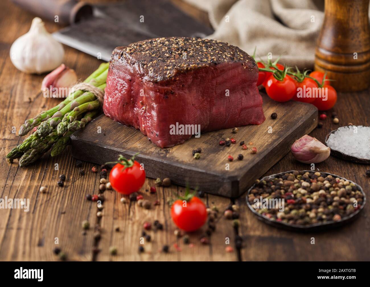 Boeuf tende de tranche de joint avec du sel et du poivre sur la planche à découper en bois avec des tomates de l'ail et d'asperges sur table de cuisine en bois. Banque D'Images