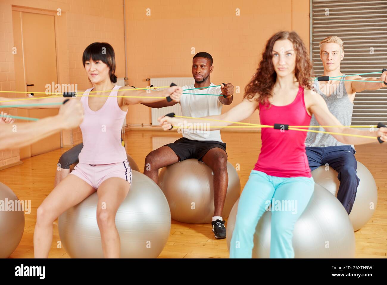 Groupe dans la salle de gym assis tout en s'étirant sur des balles d'exercice Banque D'Images