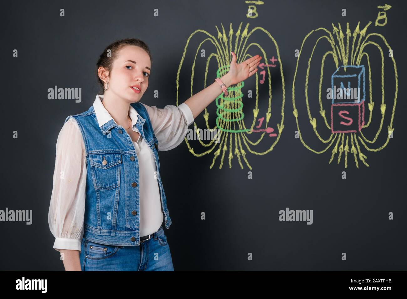Jeune professeur de physique de femme parle des champs magnétiques, expliquant le sujet à partir de photos en couleur avec craie sur un tableau noir Banque D'Images