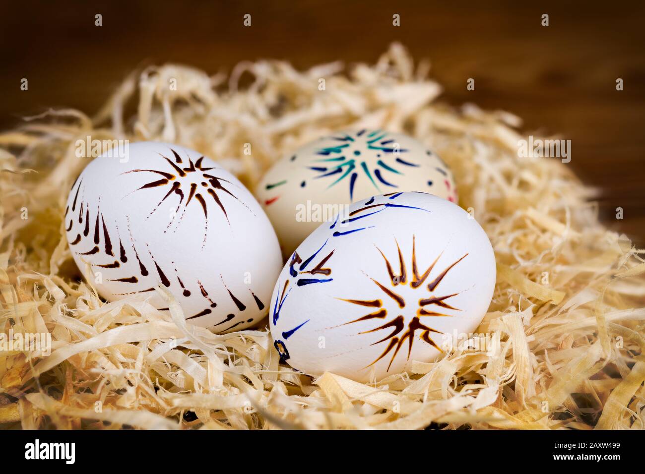 Trois œufs de Pâques ornés au nid de copeaux de bois sur fond flou. Coquilles vides à motifs décontractées peintes par la technique de cire dans la vie artistique. Banque D'Images