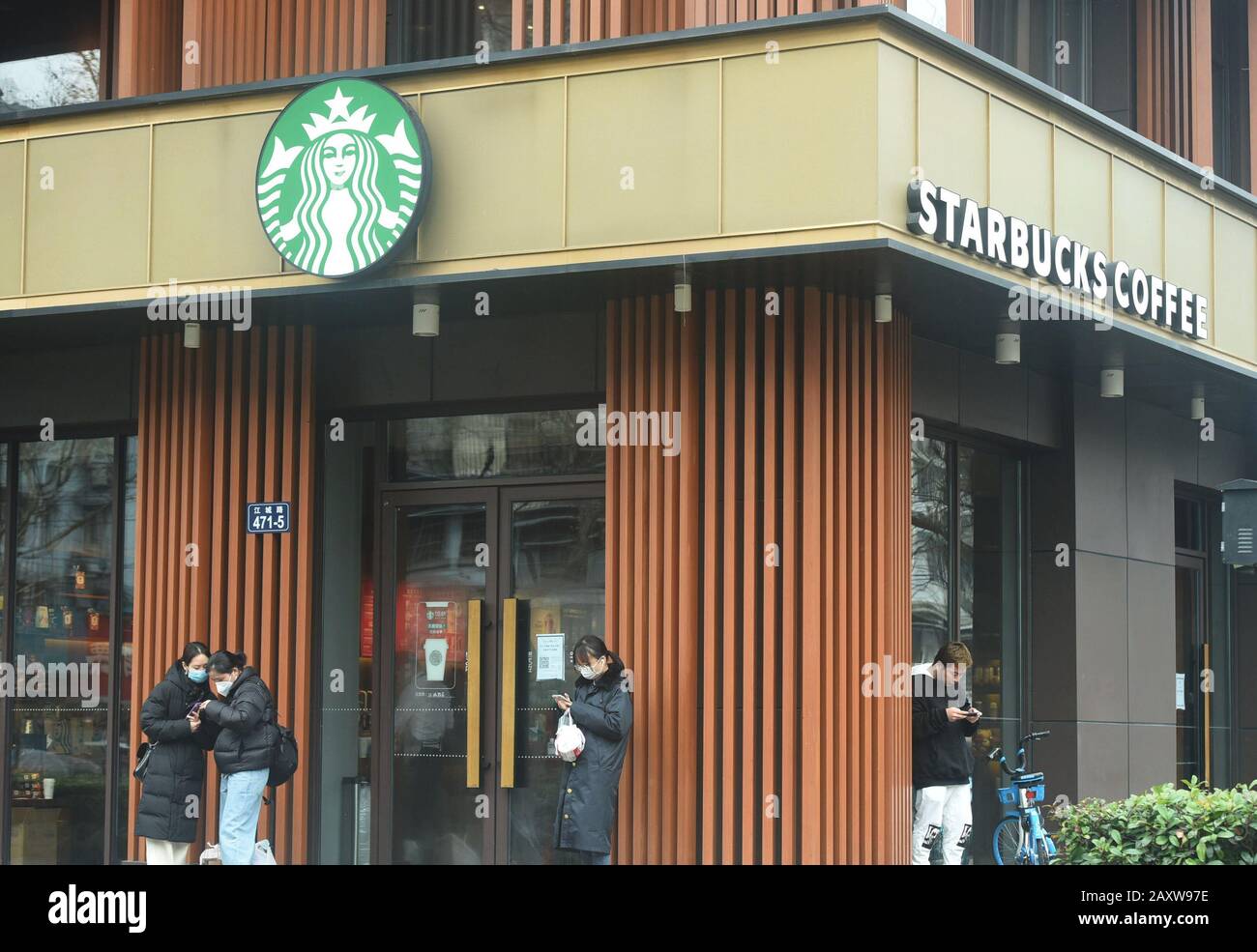 Les clients chinois portant des masques pour la prévention du nouveau coronavirus et de la pneumonie se font attendre à l'extérieur d'un café Starbucks pour obtenir leurs commandes de c Banque D'Images