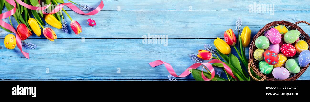 Œufs peints à Pâques dans le panier avec tulipes sur la planche bleue Banque D'Images