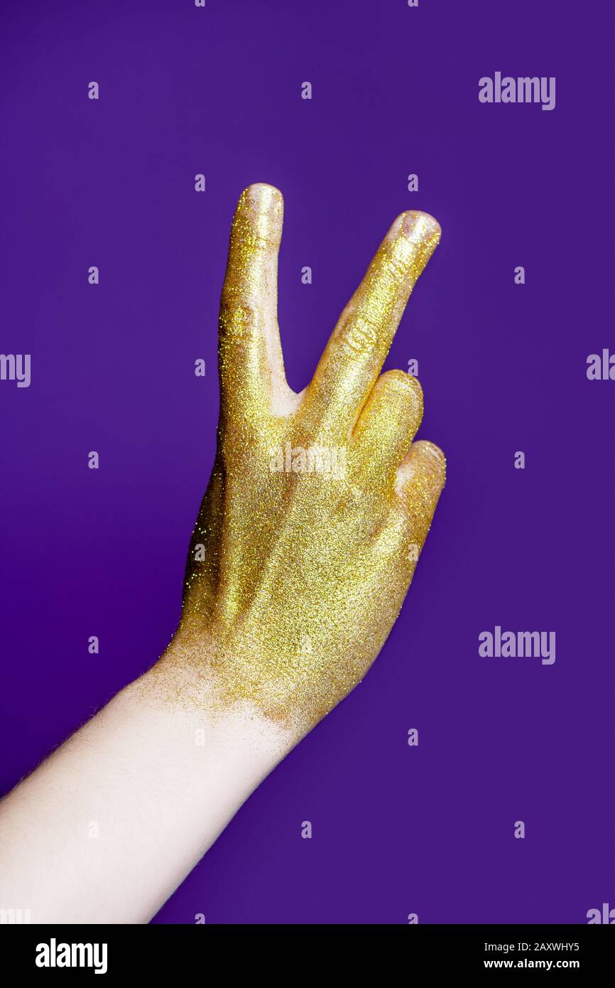 Main de l'homme avec paillettes dorées montrant le geste de victoire sur fond bleu. Banque D'Images