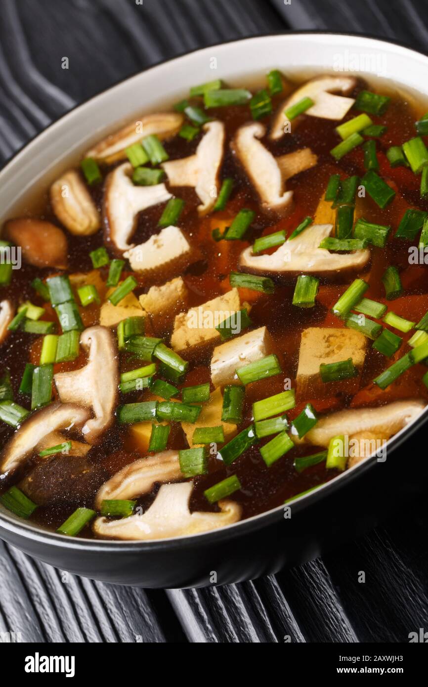 Soupe de miso japonaise avec champignons shiitake, tofu et oignons verts gros plan dans un bol sur la table. Vertical Banque D'Images