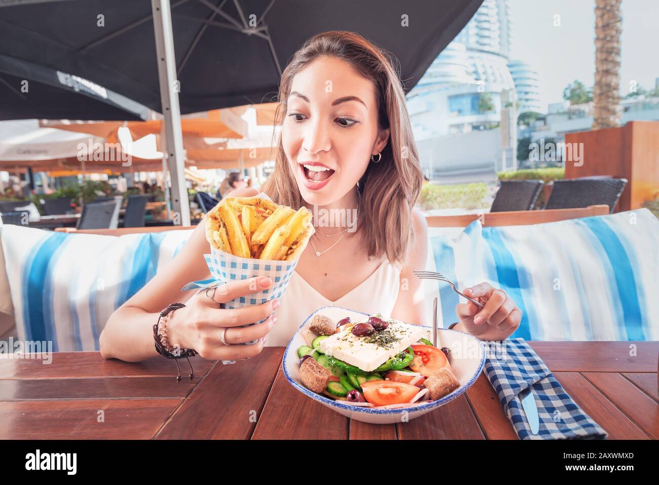 Une jeune fille touristique gaie essaie de déguster une cuisine grecque dans un restaurant local. Sur la table salade traditionnelle Horiatiki et Gyros à Pita Banque D'Images