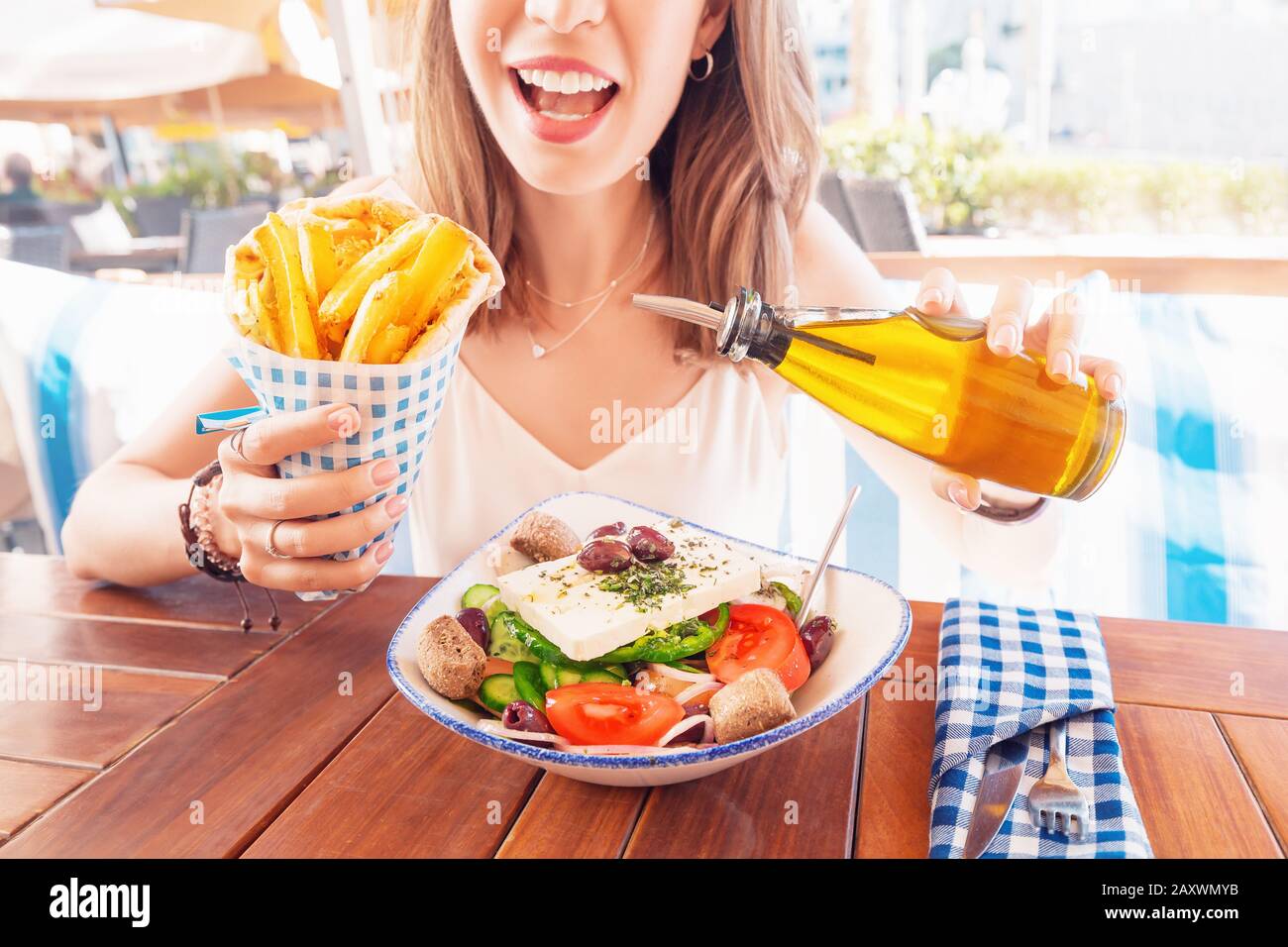 Une jeune fille touristique gaie essaie de déguster une cuisine grecque dans un restaurant local. Sur la table salade traditionnelle Horiatiki et Gyros à Pita Banque D'Images