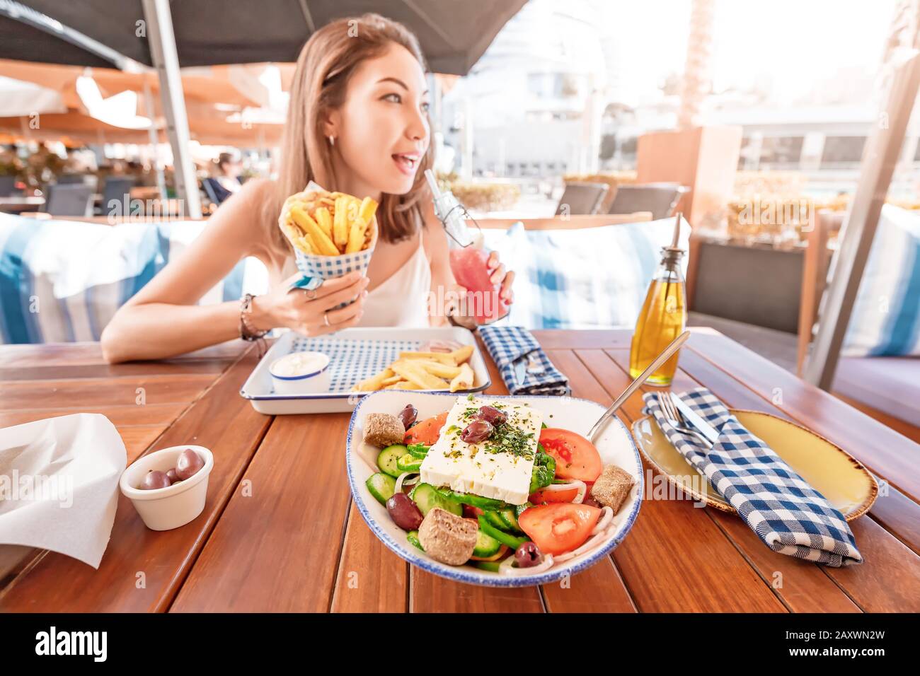 Une jeune fille touristique gaie essaie de déguster une cuisine grecque dans un restaurant local. Sur la table salade traditionnelle Horiatiki et Gyros à Pita Banque D'Images