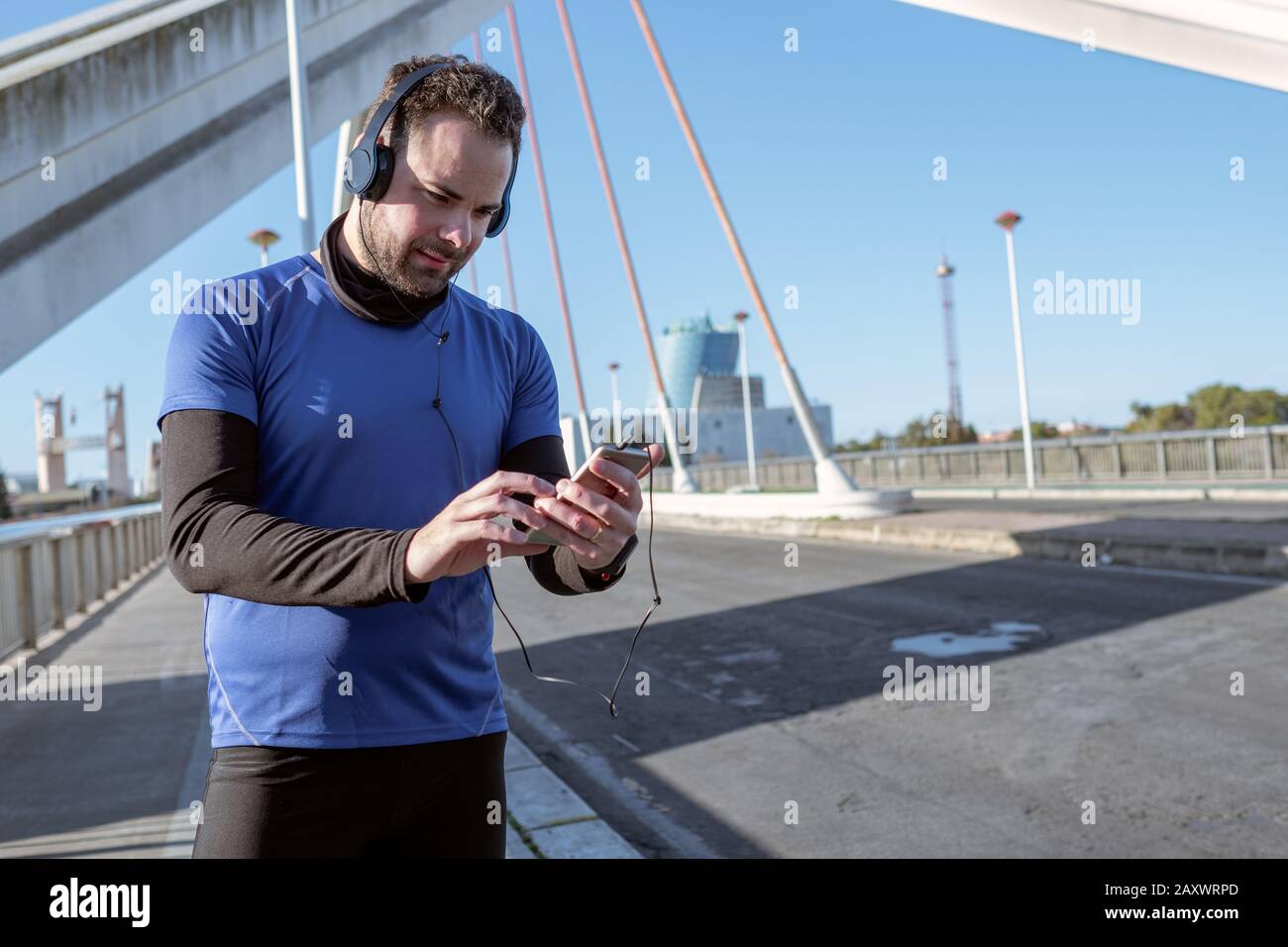 jeune homme regardant son téléphone portable pour écouter de la musique tout en traversant une zone urbaine Banque D'Images