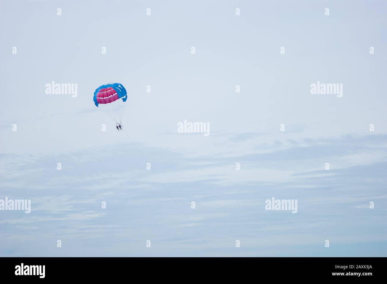 Un parachute bleu-rouge avec deux personnes dans le ciel nuageux. Extrême, été, vacances, activisme, bonheur, deux. Banque D'Images