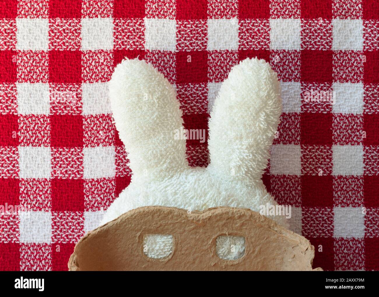 Oreilles de lapin en éponge blanches avec masque de carboard. Nappe carrée rouge en arrière-plan. Pâques et carnaval. Banque D'Images