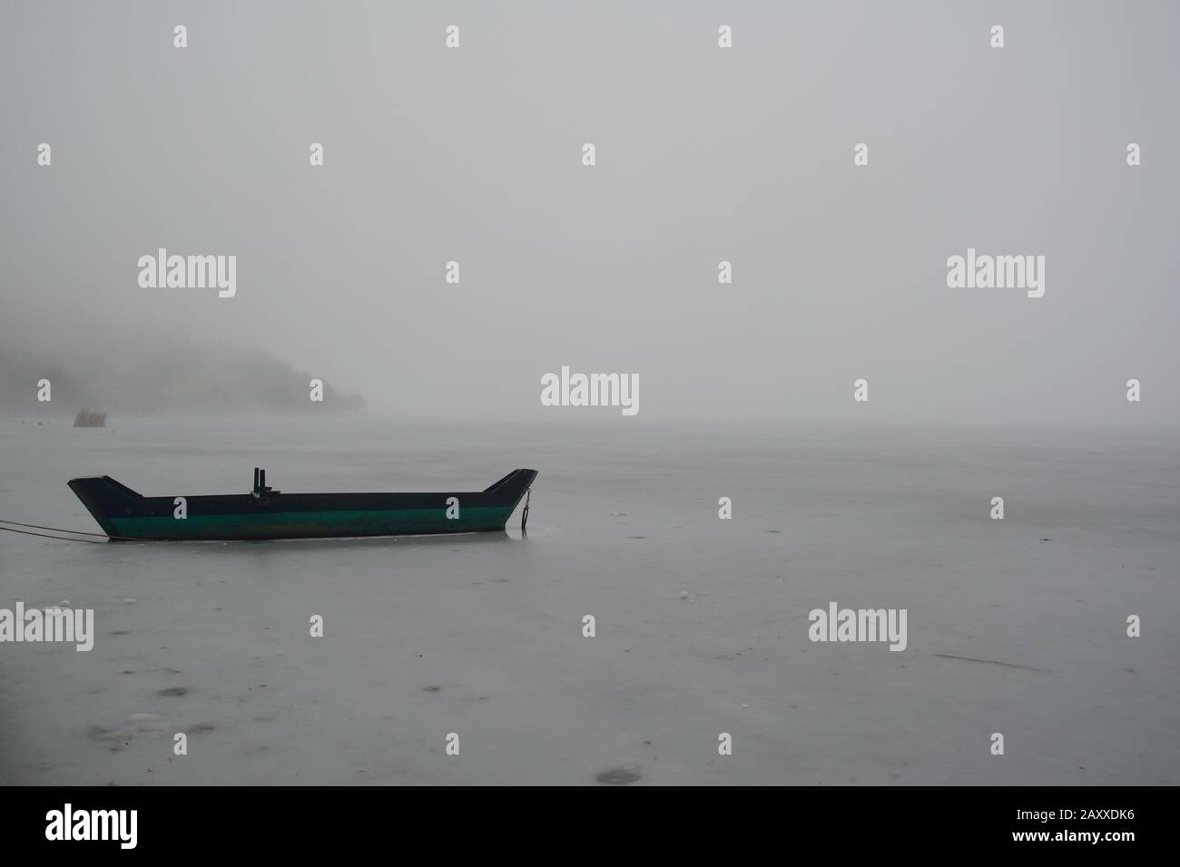 Paysage avec un bateau en bois dans le lac gelé une journée brumeuse Banque D'Images
