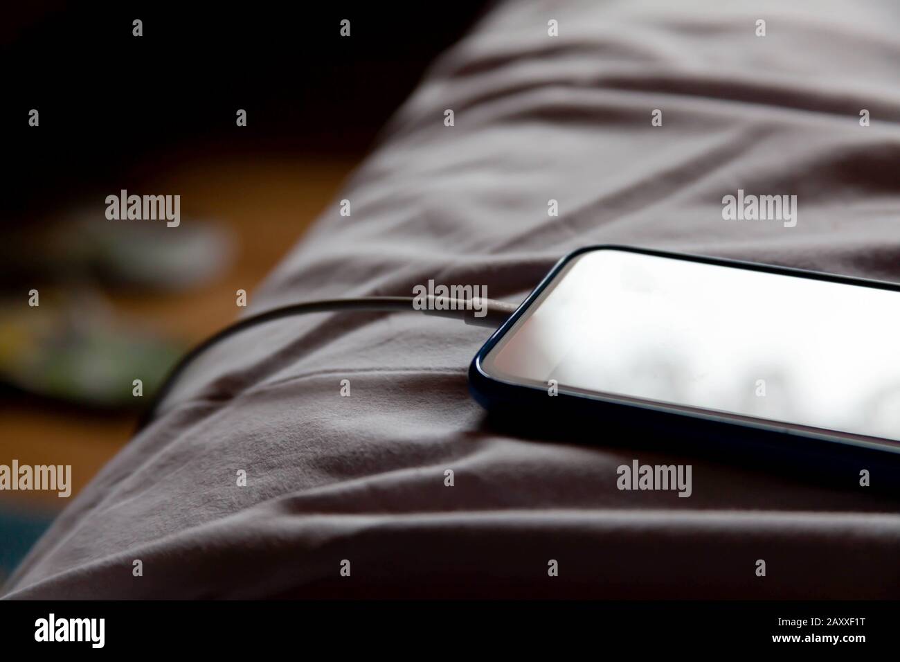Un simple moderne sans nom smartphone posé dans le lit dans des feuilles blanches froissés charge le matin, closeup. Arrière-plan de la chambre. Quitter un appareil téléphonique Banque D'Images
