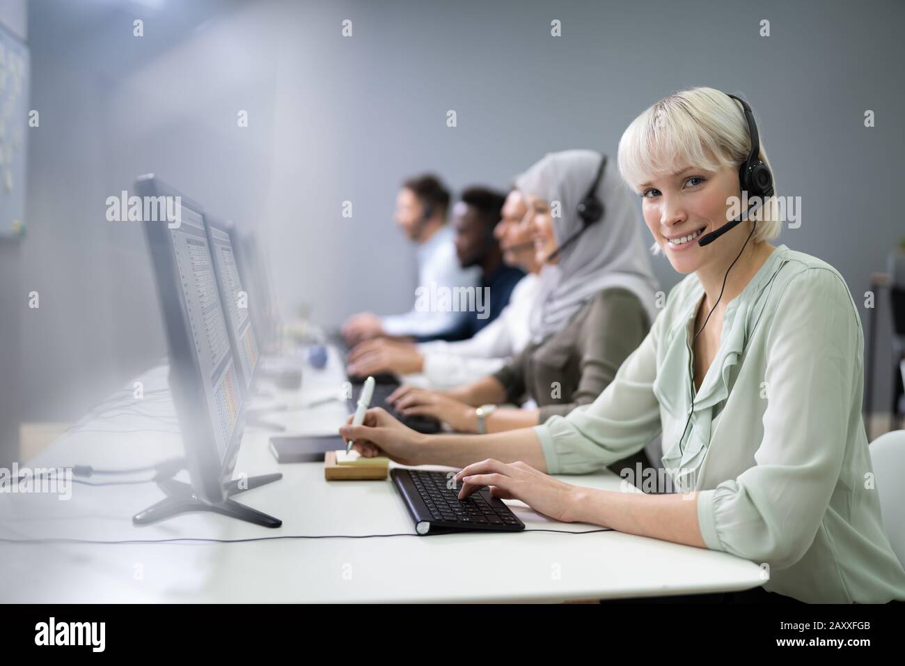 L'agent des services à la clientèle féminine positive avec casque de travail dans un centre d'appels Banque D'Images