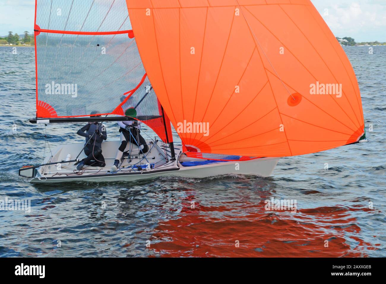 Deux enfants naviguant sur un canot de course avec un grand spinnaker de couleur orange entièrement déployé pour s'amuser et en compétition. Travail d'équipe pratiqué. Banque D'Images