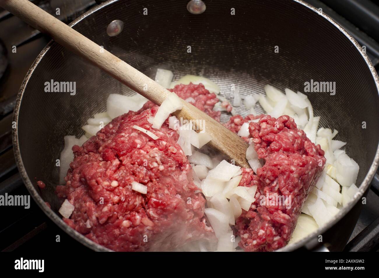 Dorer la viande de bœuf et les oignons frais en dés dans une casserole sur  une table de cuisson à gaz à l'aide d'une cuillère en bois, gros plan dans  la casserole