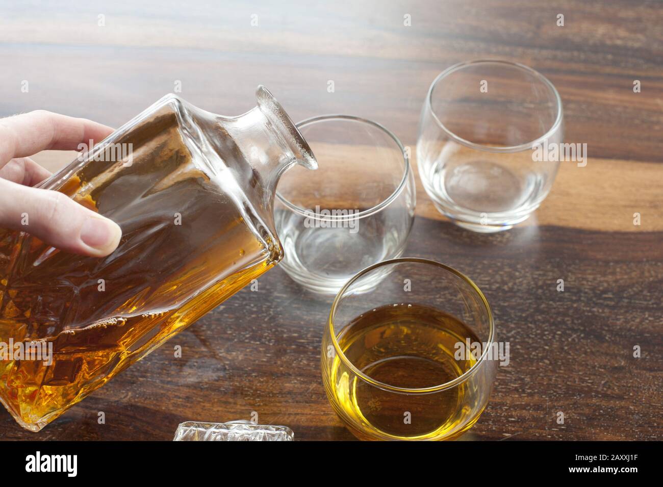 Homme qui verse des verres de whisky à partir d'un décanteur de verre sur un comptoir de bar en bois, vue rapprochée de sa main Banque D'Images