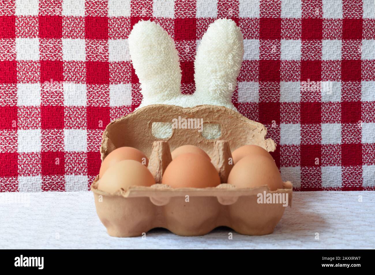 Oreilles de lapin en éponge blanches avec masque de carboard et œufs. Fond blanc et rouge à damier et nappe en dentelle blanche Pâques et carnaval. Banque D'Images