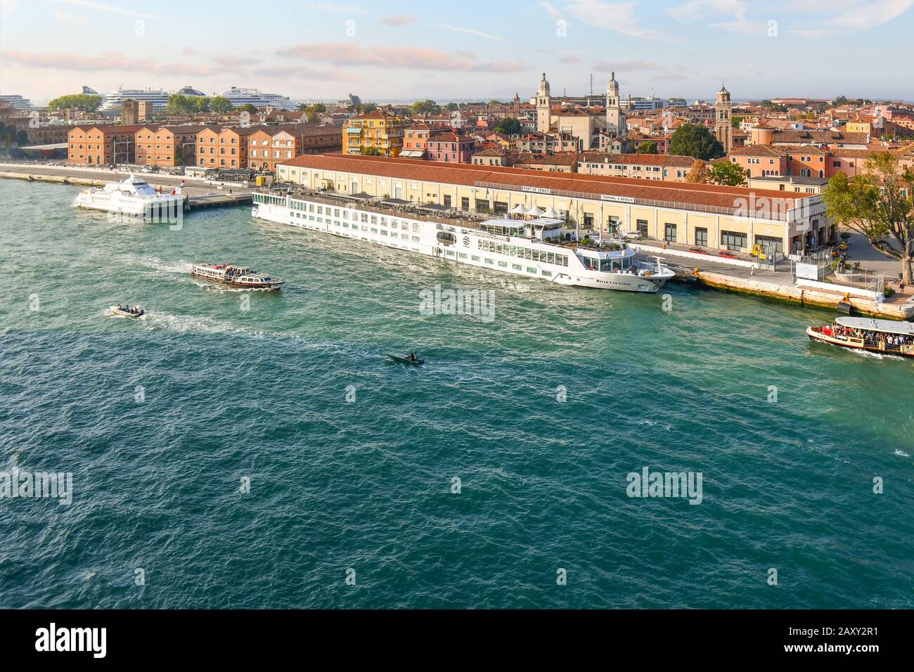 Un petit bateau de croisière sur le fleuve arrime à un port de Venise avec  les grands bateaux de croisière vus à la distance derrière au port  principal du navire Photo Stock -