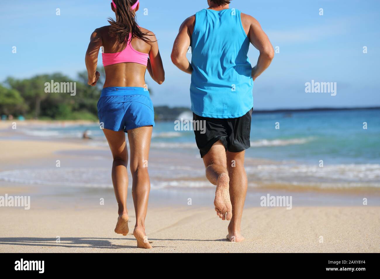 Deux athlètes coureurs couple courir ensemble sur la plage. Les gens de derrière le jogging loin pieds nus sur le sable sur la destination de voyage tropicale. Bas du corps, jambes, pieds. Banque D'Images