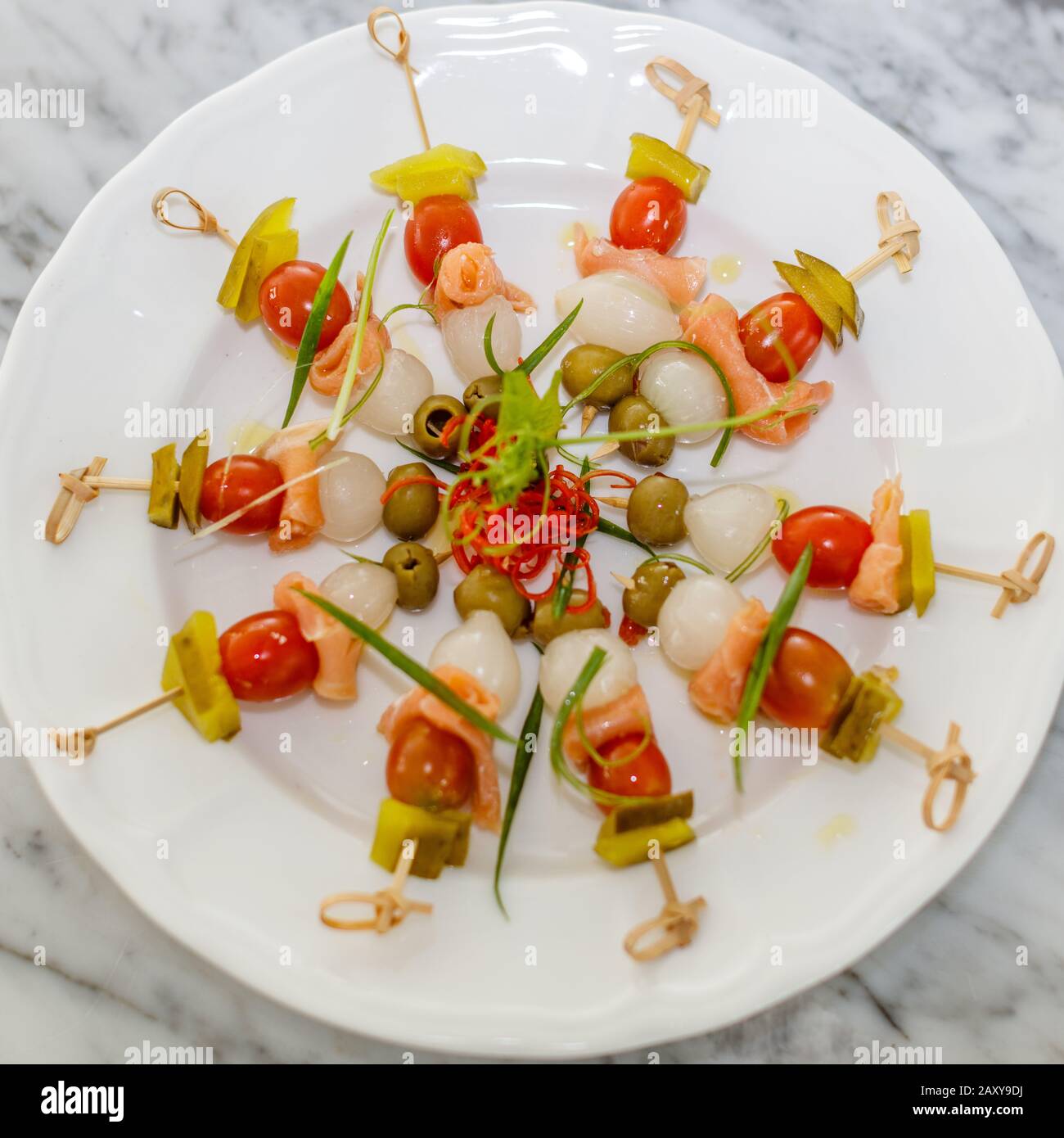 Brochettes de bambou avec oignon mariné, saumon salé, olives vertes, cornichons et tomates cerises. Apéritif à cocktail. Servi sur une plaque en céramique blanche. Banque D'Images