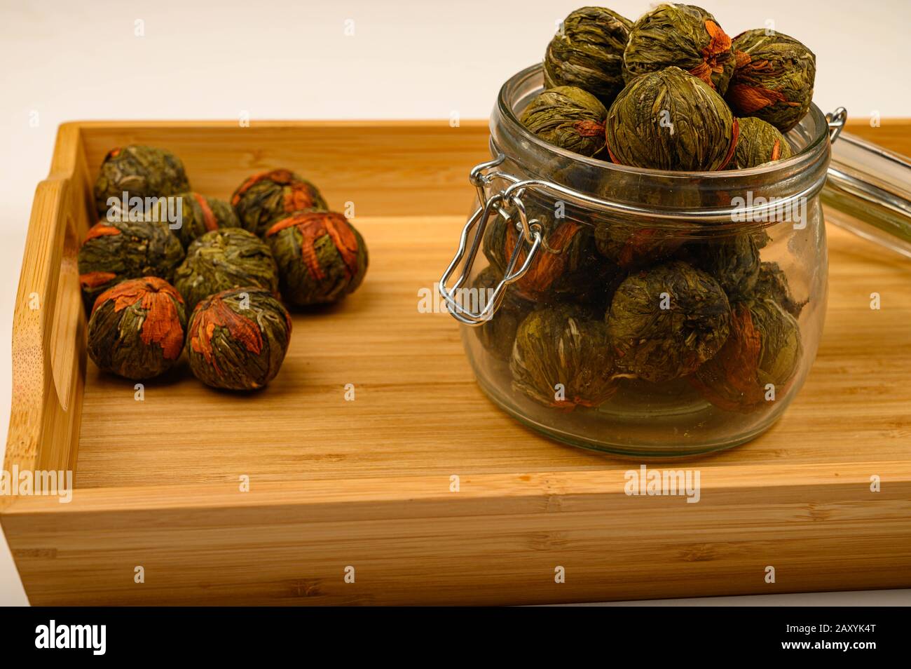 Une boule de thé de fleur dans un pot en verre sur un plateau en bois sur un fond blanc. Gros plan Banque D'Images