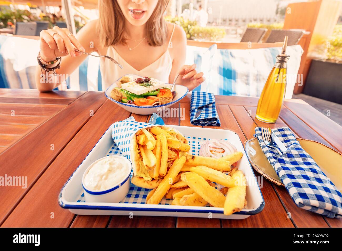 Une jeune fille touristique gaie essaie de déguster une cuisine grecque dans un restaurant local. Sur la table salade traditionnelle Horiatiki et Gyros à Pita Banque D'Images