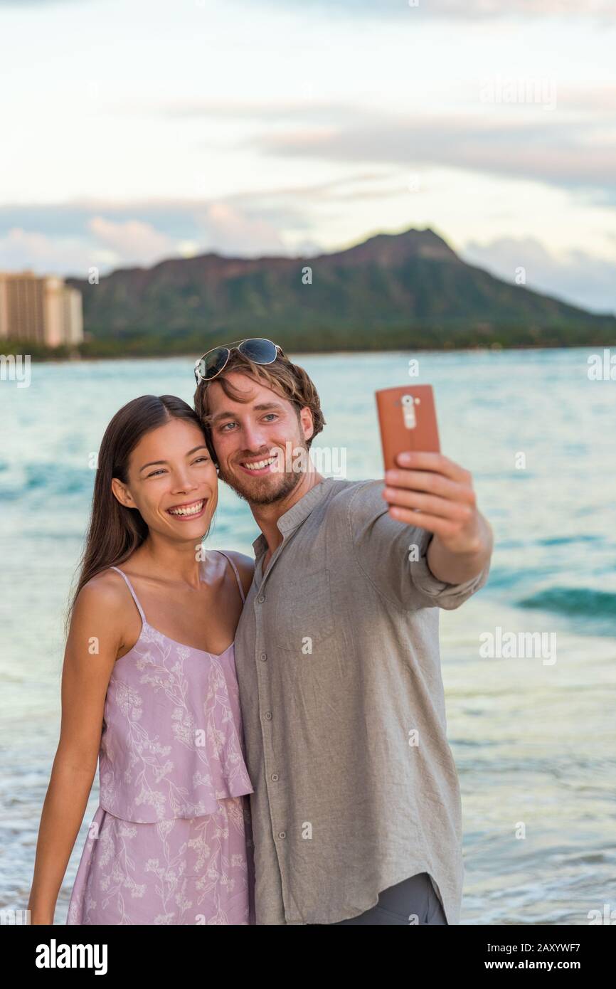 Couple prenant téléphone selfie sur la plage de Waikiki au coucher du soleil, Honolulu, Hawaii voyage vacances. Jeunes en vacances hawaïennes. Destination romantique pour lune de miel. Banque D'Images