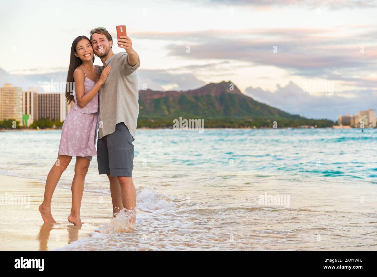 Couple marchant sur la plage au coucher du soleil en prenant la photo de selfie sur le téléphone mobile se relaxant ensemble sur Waikiki Beach, Honolulu, Hawaï Voyage vacances. Destination romantique pour lune de miel. Banque D'Images