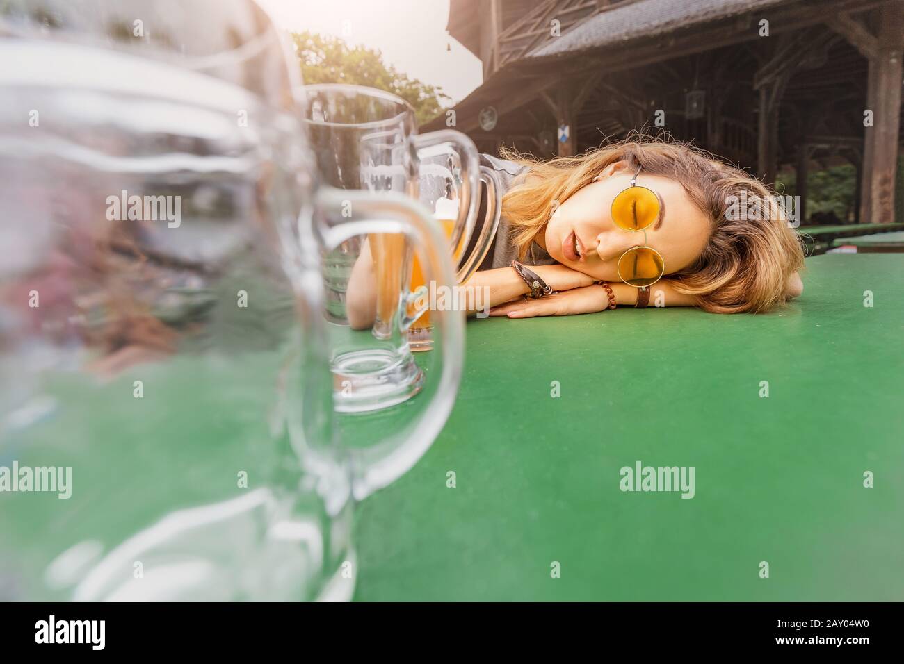 Jeune fille asiatique ivre avec gueule dormant à Biergarten avec des tasses à bière vides Banque D'Images