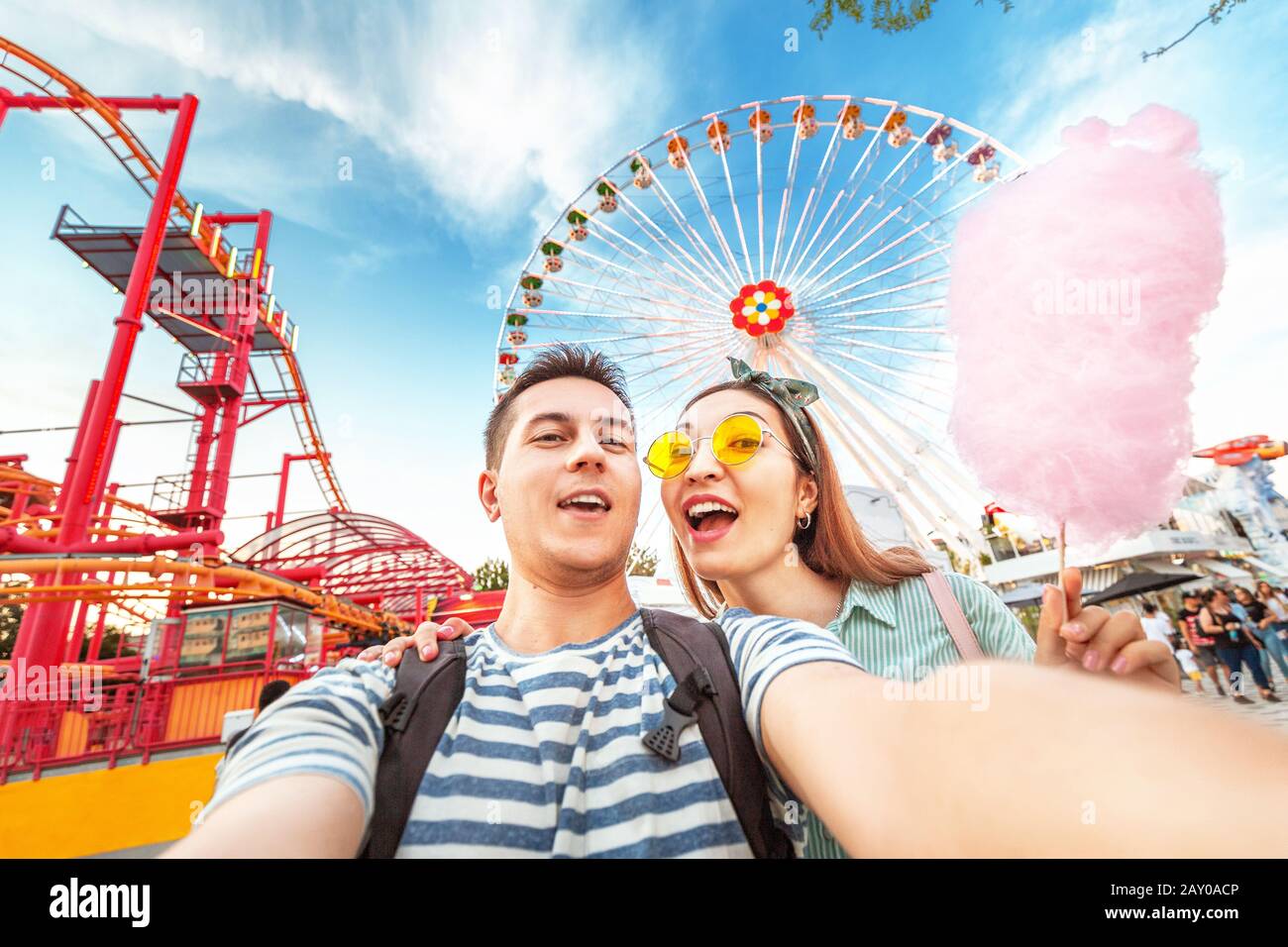 Couple de course mixte affectueux embrassant et mangeant des bonbons de coton et prendre selfie pendant le week-end au parc d'attractions. Date et relation Banque D'Images