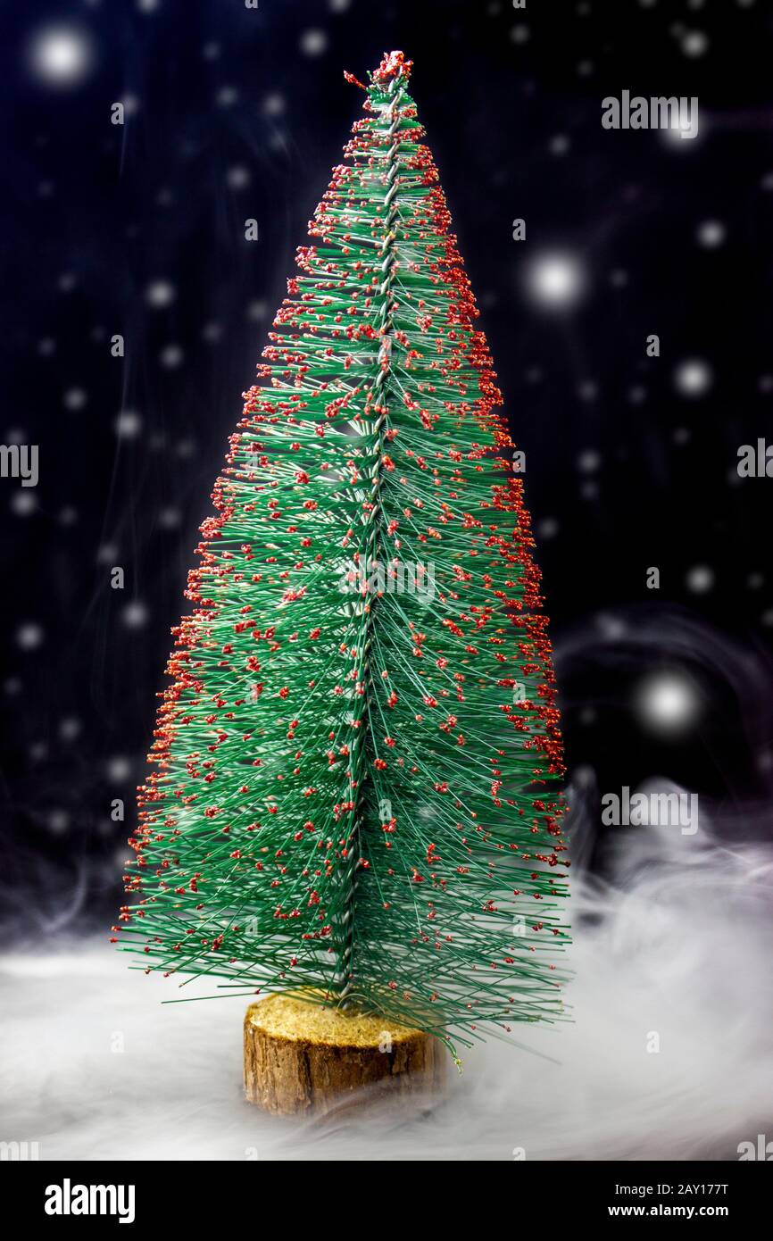 Arbre de Noël sur fond noir et neige, tempête de neige et neige sur fond sombre. Arbre de Noël décoratif miniature. Banque D'Images