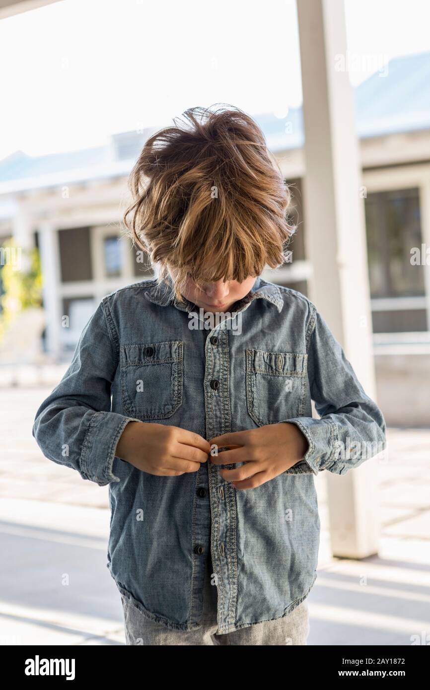 un garçon de 6 ans a boutonné sa chemise en denim Banque D'Images