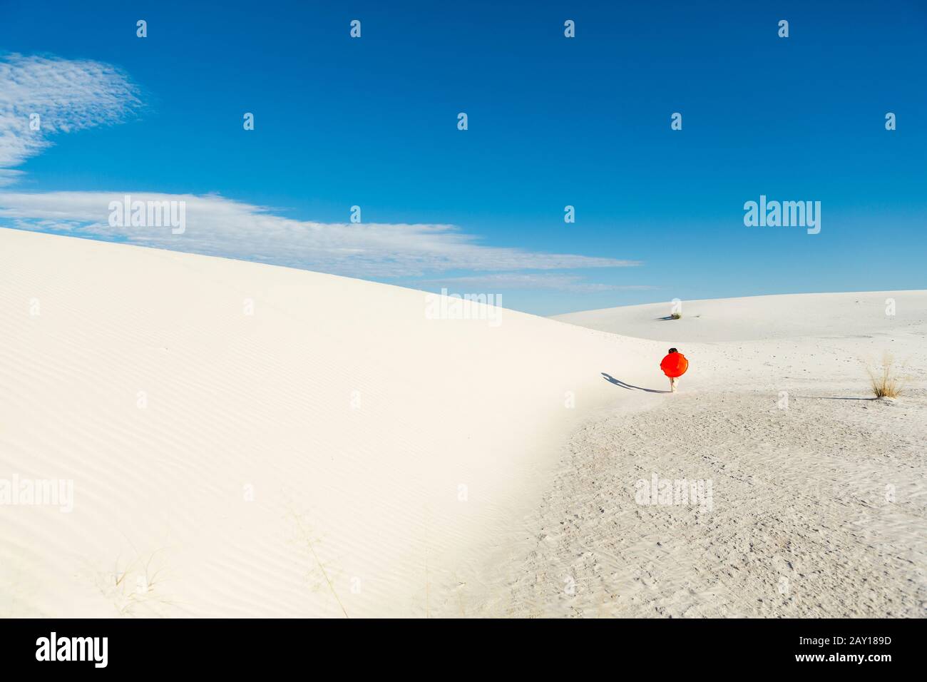 garçon de 6 ans portant un traîneau orange dans un paysage de dunes ondulées blanches. Banque D'Images