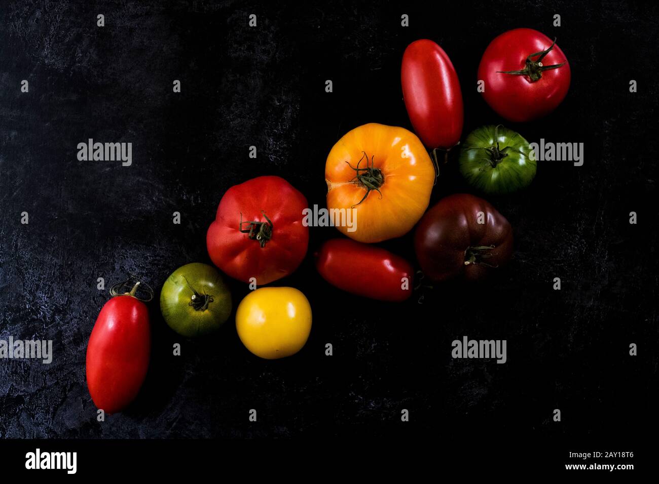 Grand angle gros plan d'une sélection de tomates dans différentes formes et couleurs sur fond noir. Banque D'Images