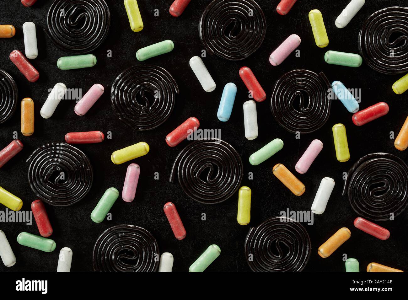 Bobines noires de réglisse avec de longues bonbons à la réglisse couchés de sucre sur un fond noir dans un modèle plein format de gros plan Banque D'Images