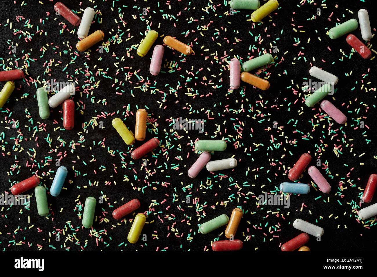 Texture d'arrière-plan des bonbons sur fond noir avec des saupoules de cuisson éparpillées et de la réglisse enrobée de sucre dans un motif aléatoire Banque D'Images