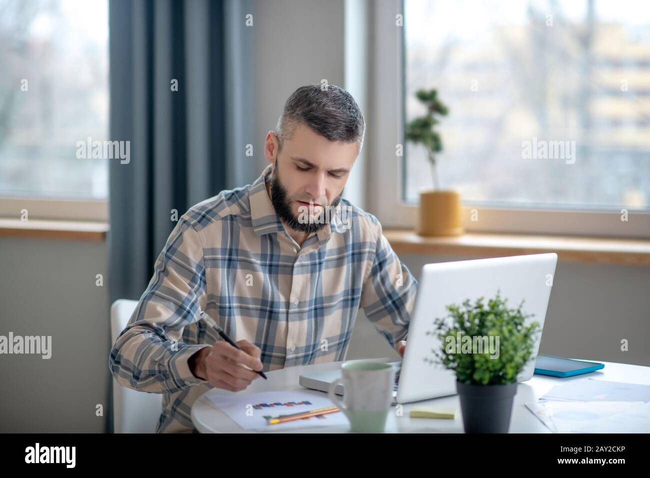 Jeune homme barbu assis et travaillant avec un tableau. Banque D'Images