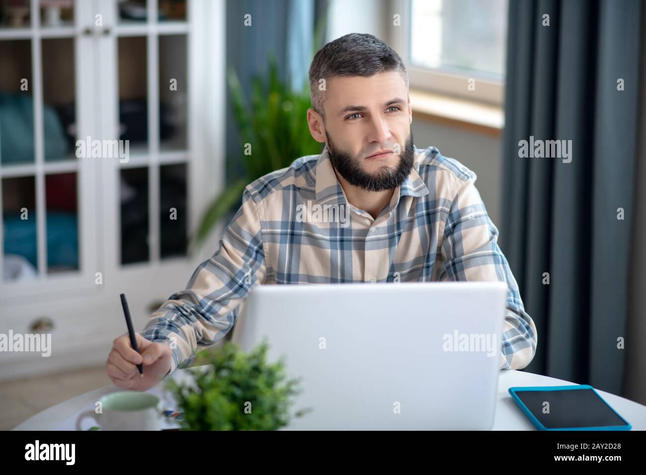 Jeune homme aux cheveux sombres qui travaille derrière un ordinateur portable blanc. Banque D'Images