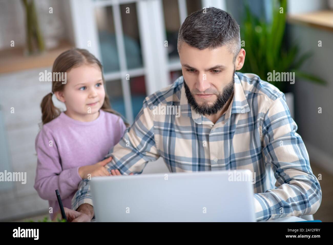 Jeune père sérieux à l'ordinateur portable, petite fille regardant papa. Banque D'Images