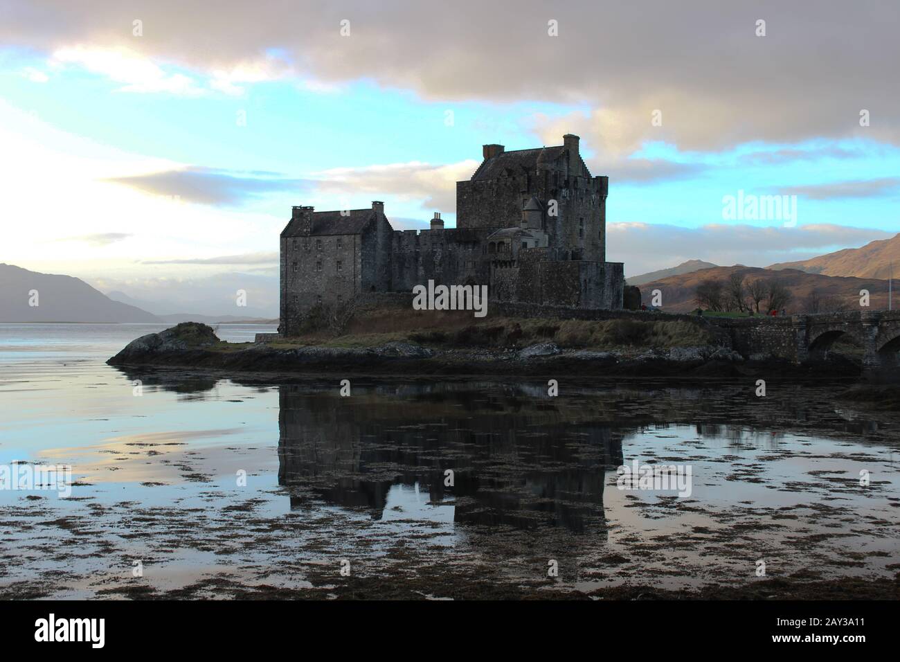Le superbe château d'Eilan Donan se reflète parfaitement dans les eaux écossaises lors d'une journée encore surpassée avec le soleil qui frappe les collines Banque D'Images