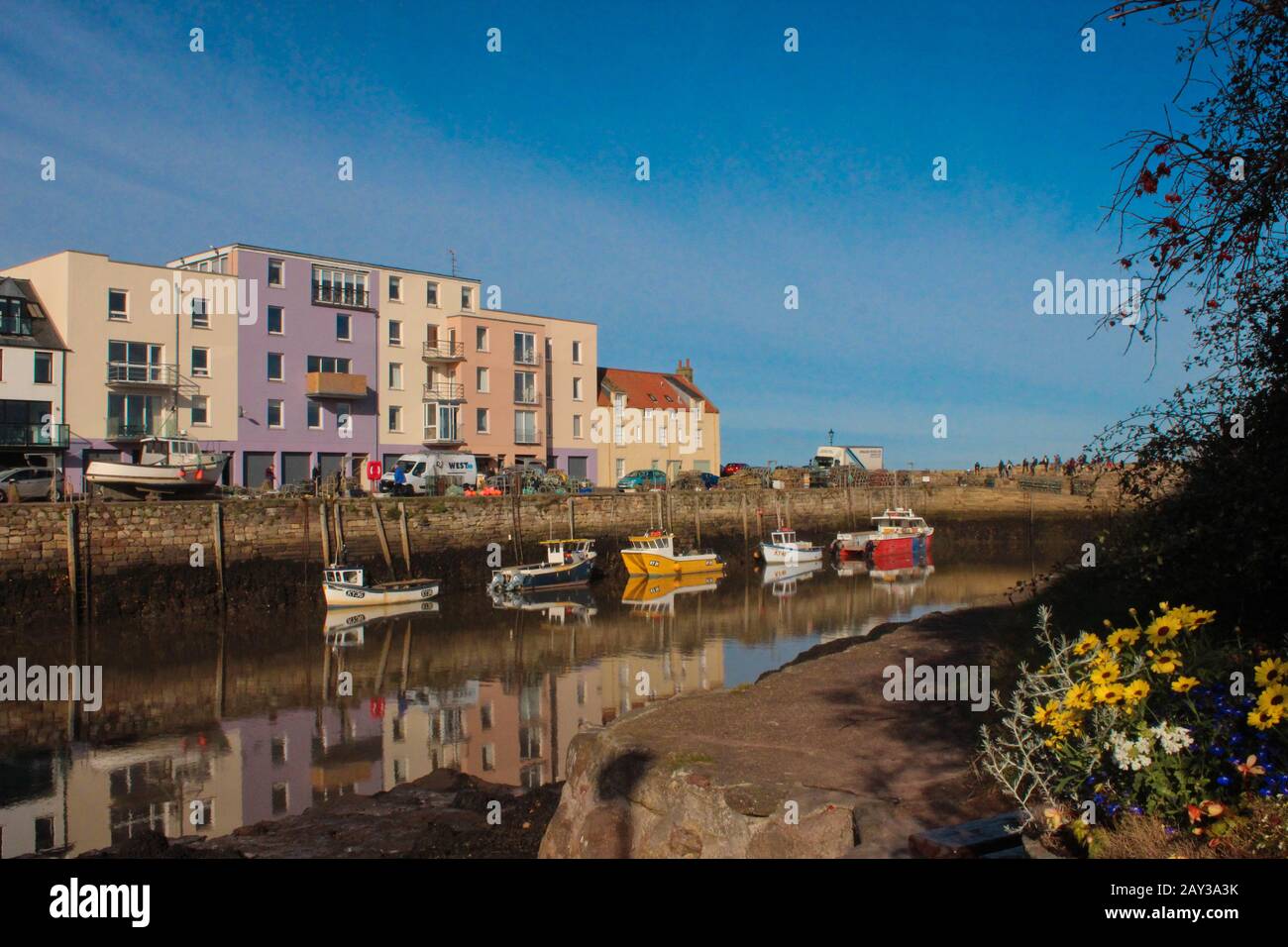 Vue imprenable sur les étudiants de St Andrews assis sur la jetée à côté du port et une journée ensoleillée après la rason avec des fleurs colorées et des bateaux de pêche Banque D'Images