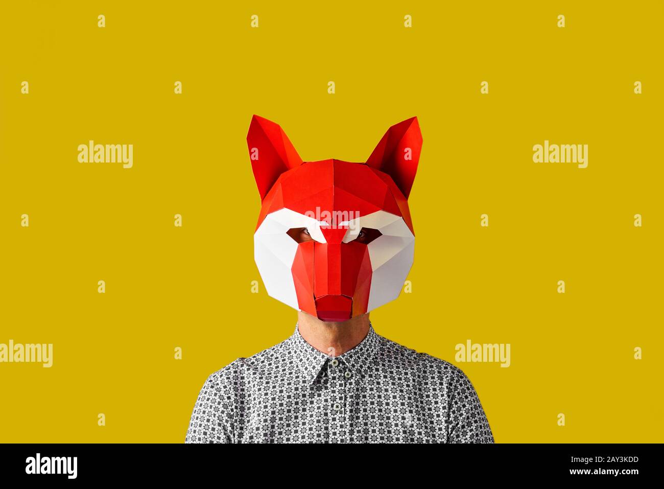 jeune homme caucasien portant un masque de renard rouge et blanc sur un fond jaune avec un espace vide autour de lui Banque D'Images