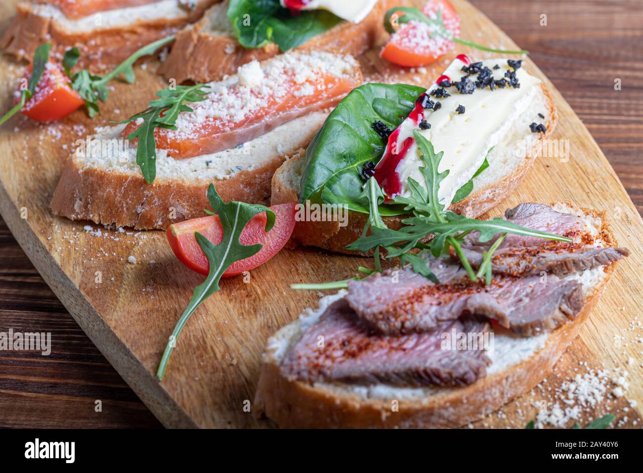 Sandwichs au poisson rouge, au bœuf en suvit et au fromage doux. Garnies de tranches de microvert, d'arugula et de tomates. Sur un plateau ovale en bois espace de copie Banque D'Images
