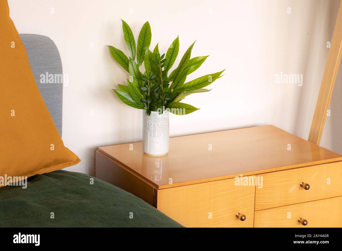 Détail de l'intérieur moderne neutre. Bouquet de feuilles fraîches de vert clair debout sur un bord en bois à côté du lit. Décoration simple et fraîche à motif fleuri Banque D'Images