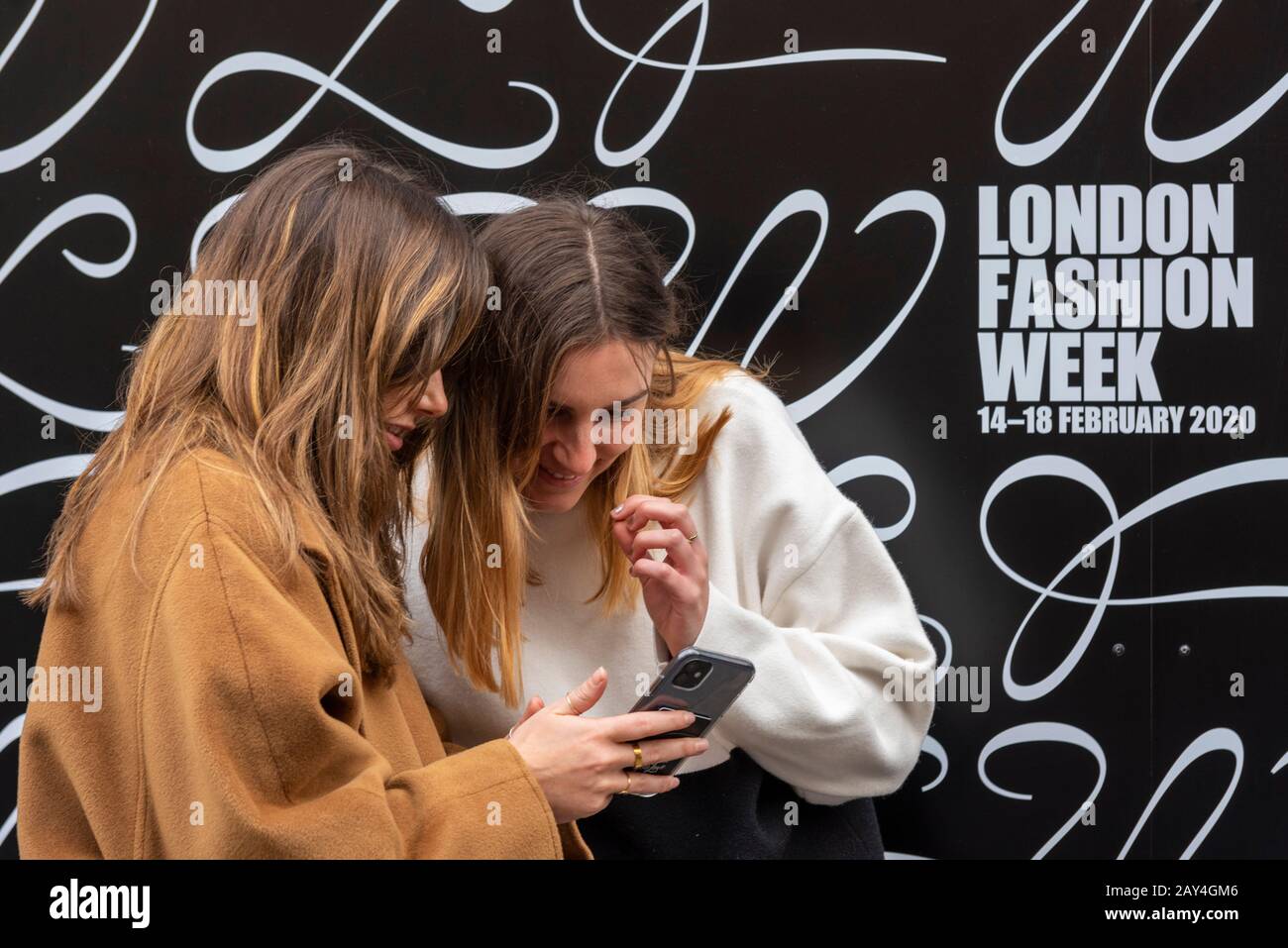 Strand, Londres, Royaume-Uni. 14 février 2020. La London Fashion week 2020 a commencé au magasin X dans le Strand. Les modèles et les visiteurs ont été tendues leurs trucs dans les rues à l'extérieur comme fashionistas et le public arrivent. Deux femmes intéressées par le téléphone mobile par logo de marque Banque D'Images