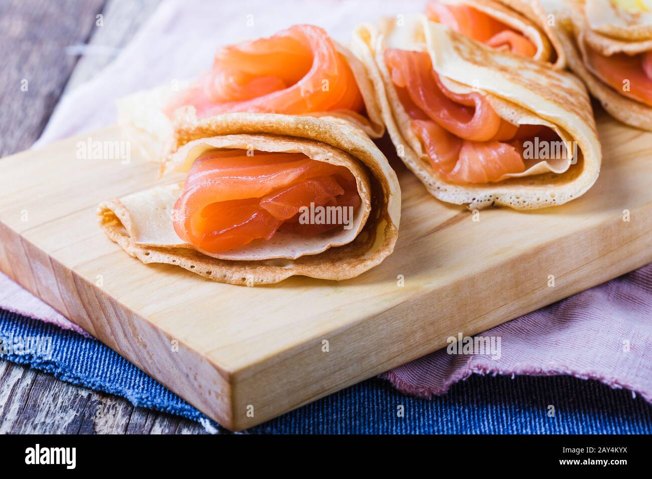 Blini de style russe avec saumon fumé, apéritif traditionnel sur planche à découper en bois, cuisine folklorique de Maslenitsa, semaine de crêpes, gros plan Banque D'Images